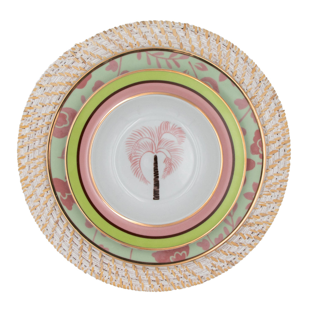White rattan charger plate with woven texture holding three stacked ceramic plates featuring pastel green, pink, and floral patterns with gold trim and a palm tree motif.