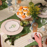 Table set with white plates featuring green hot air balloon designs on woven white rattan chargers, green scalloped placemats, and a centerpiece of desserts with orange slices and yellow flowers.