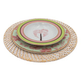 Stack of three decorative plates featuring tropical and floral motifs in pink, green, and gold, placed on a round white woven rattan charger.