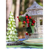 White woven rattan pagoda lantern adorned with red berries and green leaves, next to a textured green and white pine tree ornament on an outdoor table.