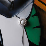 Close-up of a wall-mounted white round ceramic button switch on a colorful painted background with abstract shapes in green, gray, black, and orange.