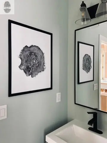Black-and-white print of a detailed Williamsburg, Virginia oak tree cross-section displayed in a black frame on a light gray bathroom wall above a white sink with a black faucet, reflected in a mirror.