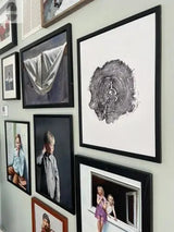 Wall displaying various framed artworks including a black and white cross-section print of an oak tree, portraits of children, a draped fabric, and a bearded man.
