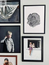 Wall display of five framed artworks including a gray-toned draped cloth, black and white oak tree cross-section print, portrait of a blonde child in gray coat, two girls sitting at a window, and a bearded man portrait.