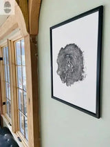 Black and white print of an oak tree cross-section with visible growth rings, framed in black and hanging on a light green wall near wooden window frames.