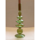 Curved green glass candle holder with stacked rounded shapes and scalloped base, holding a brown taper candle against a beige background.
