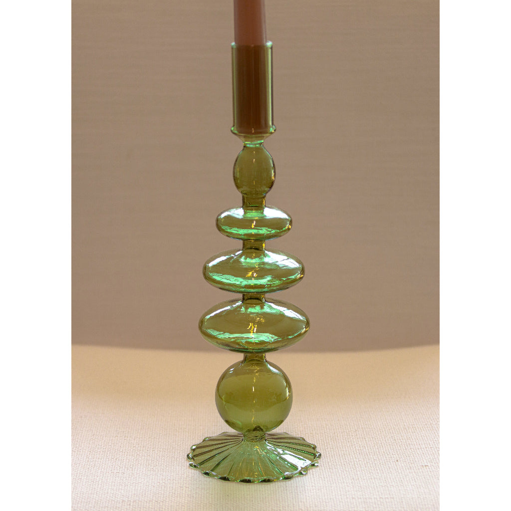 Curved green glass candle holder with stacked rounded shapes and scalloped base, holding a brown taper candle against a beige background.