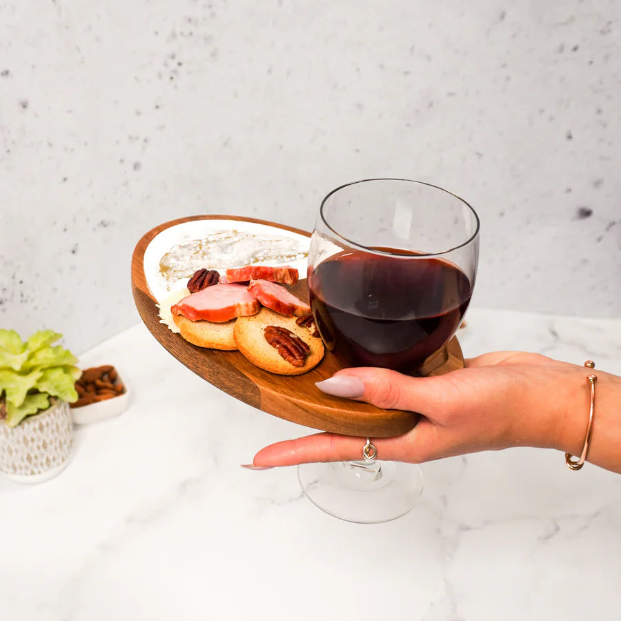 Hand holding a glass of red wine with a Wine & Appetizer Tray of snacks on a light background