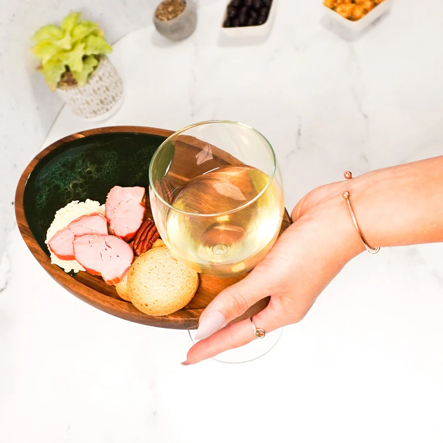 Hand holding a glass of white wine with a plate of food on a resin Wine & Appetizer Tray