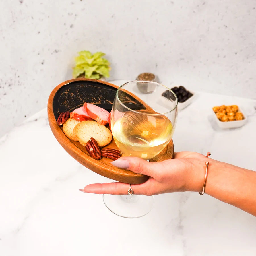 Hand holding a glass of white wine with a Wine & Appetizer Tray of snacks on a light background