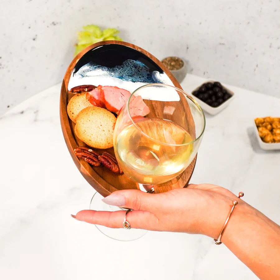 Hand holding a glass of white wine with a Wine & Appetizer Tray in the background