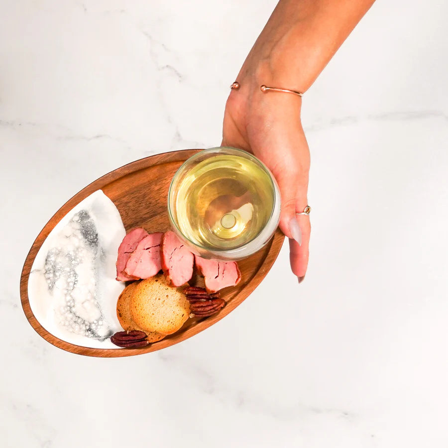 Hand holding a glass of white wine over a Wine & Appetizer Tray with food on a light background