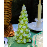 Green translucent pine tree figurine with frosted tips placed on a green tablecloth surrounded by woven basket, white candle, and glass plates with green rims.