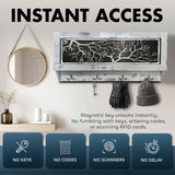 Wall-mounted rectangular cabinet with white distressed frame and black panel featuring white tree branch design; three hooks below holding gloves, hat, and a dangling key.