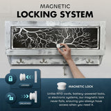 Hand turning white magnetic lock knob on rectangular black panel with white tree branch design, part of a distressed white wooden wall-mounted key holder with four hooks.