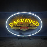Oval neon sign with a white border and yellow word 'DEADWOOD' above ornate 'TOBACCO CO.' and red 'Cigar Bar' text on black background