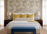 Bed with beige upholstered headboard, white bedding, and four canary yellow velvet pillows, flanked by matching wood nightstands with table lamps, set against floral wallpaper.