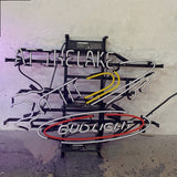 Horizontal neon sign shaped like a yacht with white, yellow, and red tubes forming the yacht and an oval around the text 'BUD LIGHT', with 'AT THE LAKE' written above in white neon tubes.