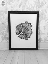 Black and white framed print of a tree cross-section showing detailed growth rings, leaning against a textured white wall on a pale wooden floor.
