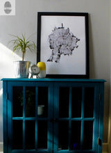 Black and white framed print of a tree cross-section showing growth rings displayed on a teal cabinet with glass-paneled doors, topped with a small clock, plant, and yellow-white object.