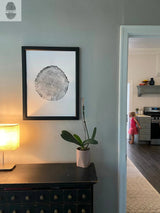 Black and white print of a tree cross-section with detailed growth rings, framed and hung on a light blue-gray wall above a black cabinet with small drawers.