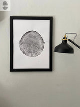 Black and white print of an oak tree cross-section with visible growth rings, framed in black and hung on a gray wall next to a black wall-mounted lamp.