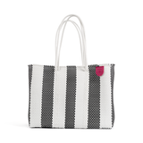 Rectangular woven tote bag with vertical black and white stripes and double white rope handles, featuring a small pink patch on the upper right corner.
