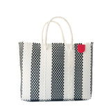 Rectangular woven tote bag with vertical black and white checkered stripes and two white handles, featuring a small red circular tag near the top edge.