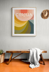 Framed modern art print with layered curved shapes in coral, mustard, olive, and teal hues, featuring the text 'Corolla North Carolina' on a light background.