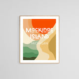 Modern art print titled 'Mackinac Island Michigan' with bold red semicircle, abstract layered shapes in beige, green, and tan, framed and displayed on a gray wall.