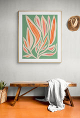 Abstract floral print with coral, pink, and white leaf shapes on a sage green background, framed and hung above a wooden bench with a white cloth draped over it.