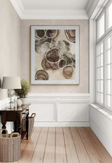 Abstract fine art print featuring layered circular sand-like textures in earthy browns, beige, and muted greens, framed in light wood against a soft beige wall.