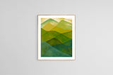 Abstract watercolor print featuring overlapping mountain shapes in shades of green and blue with a soft beige sky, framed in light wood against a gray wall.