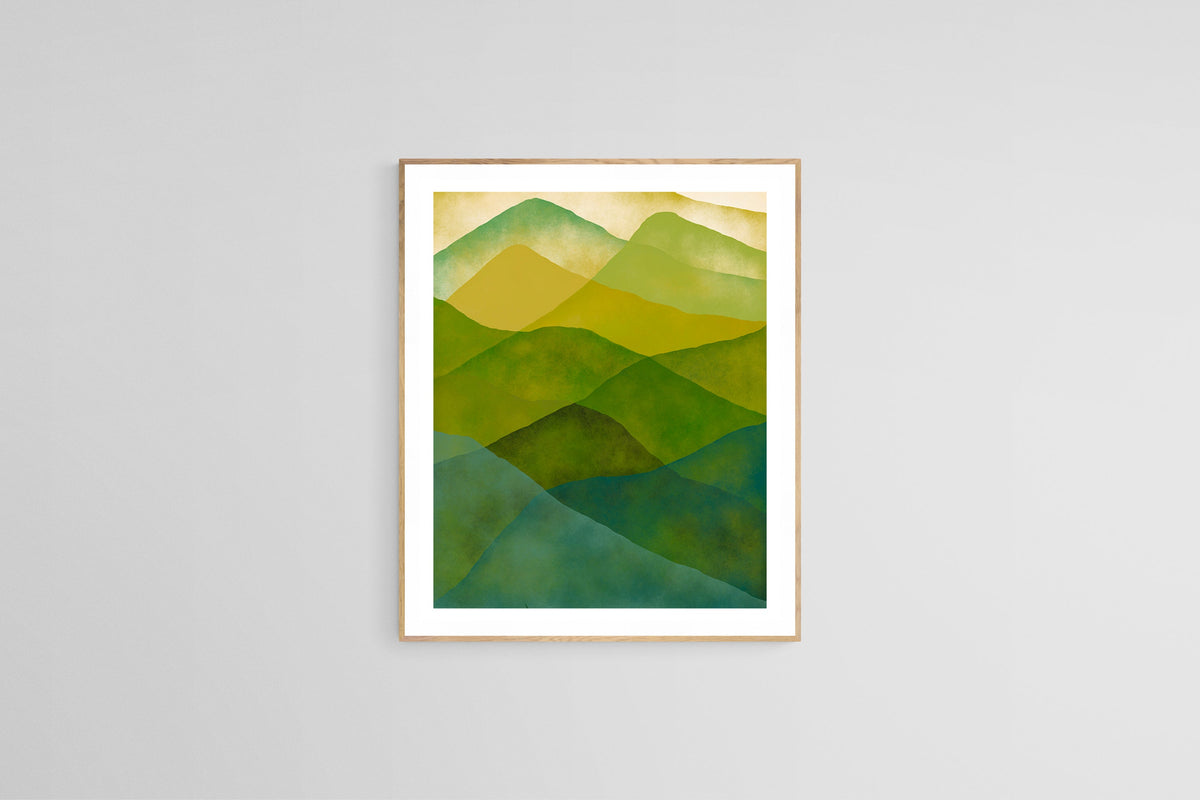 Abstract watercolor print featuring overlapping mountain shapes in shades of green and blue with a soft beige sky, framed in light wood against a gray wall.