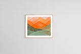 Abstract watercolor painting of overlapping mountain shapes in warm orange and cool green hues, framed in light wood and hung on a plain white wall.