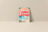 Notecard with abstract sun and sky design in peach, teal, coral, and beige hues with white script text reading 'Here Comes The Sun' on front.