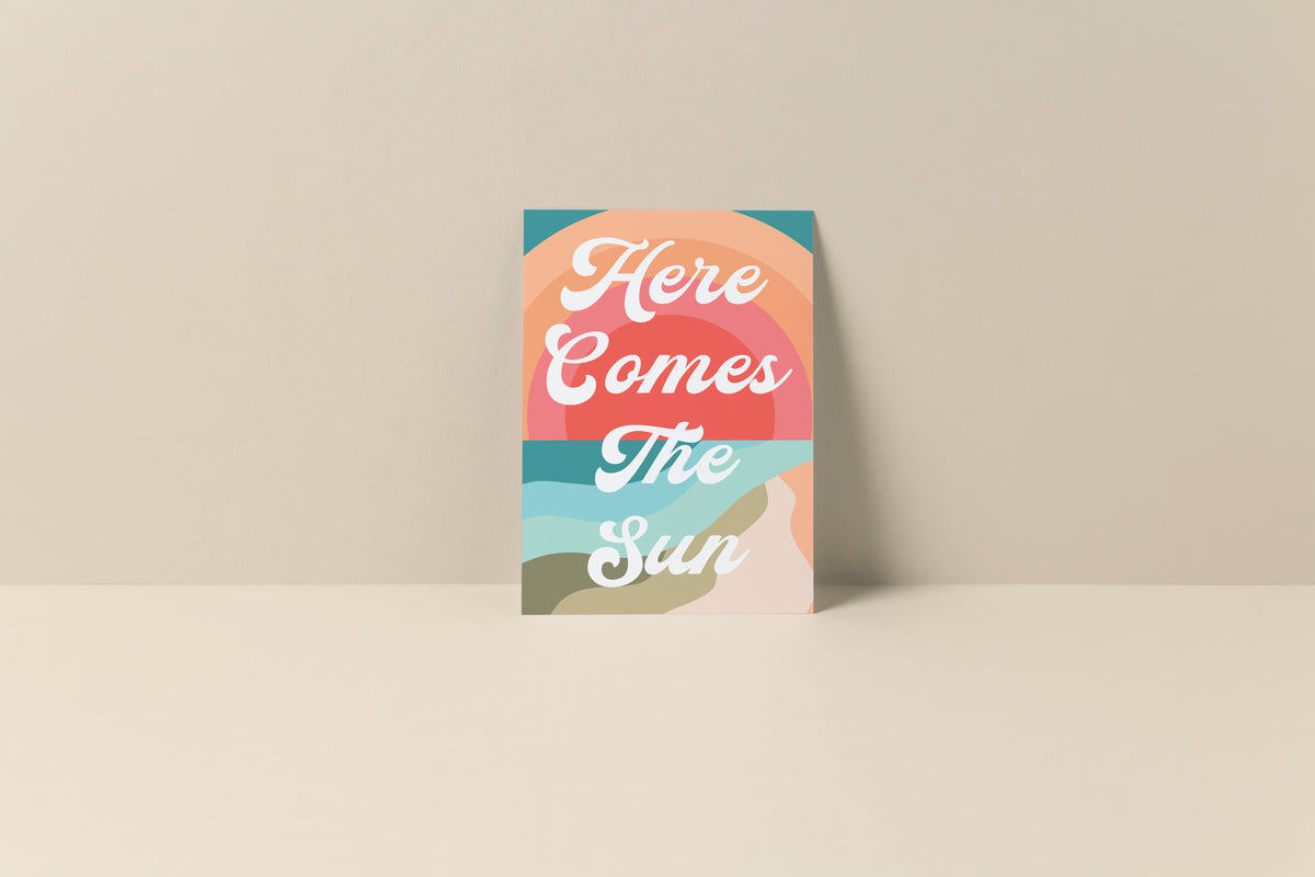 Notecard with abstract sun and sky design in peach, teal, coral, and beige hues with white script text reading 'Here Comes The Sun' on front.