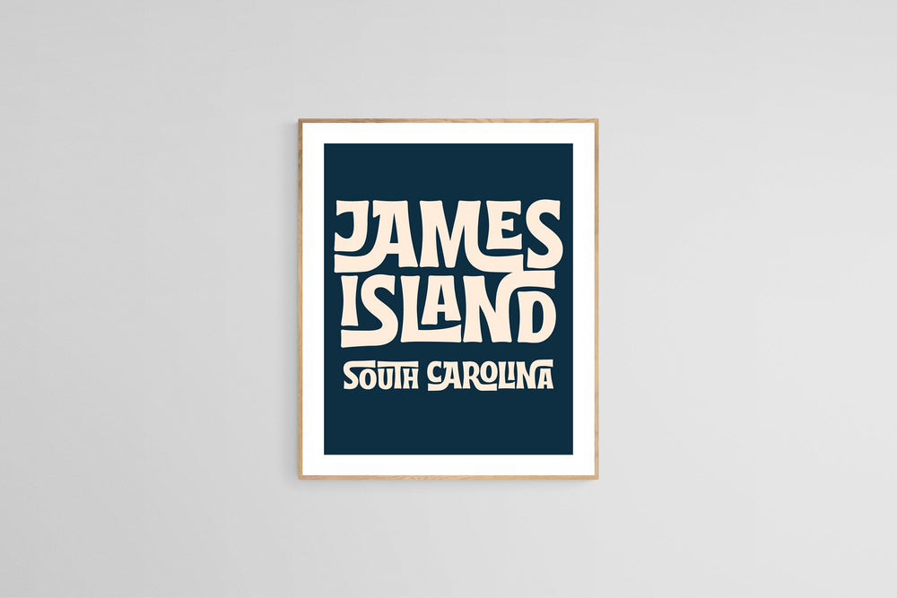 Framed modern art print with bold cream text reading 'JAMES ISLAND SOUTH CAROLINA' on a deep navy blue background, centered on a plain light gray wall.