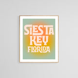 Framed modern art print with 'Siesta Key Florida' in large, stylized cream letters on a yellow-orange gradient circle against a muted teal background.