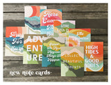 A collection of colorful note cards with layered abstract shapes in orange, green, and blue tones, each featuring inspirational phrases in white script on a wood background.