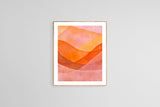 Abstract watercolor artwork depicting overlapping mountain shapes in shades of orange, pink, and red within a simple light wood frame on a gray wall.