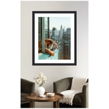 Framed photo of a tiger leaning on a balcony railing, overlooking a city skyline with tall buildings, mounted on a white wall above a green armchair and round wooden table.