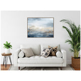 Framed abstract canvas with layered blue, beige, and gray tones resembling a misty ocean horizon, hanging above a white sofa with patterned pillows and plants nearby.