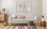 Minimalist living room with light beige modern sofa, two framed black and white floral sketches above, wooden side table, gray knitted stool, and patterned rug.