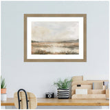 Framed neutral abstract landscape art print with soft brown, beige, and gray tones hanging above a wooden desk with a plant, black camera, and organizer