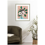 Framed floral painting titled Blush in Bloom with white flowers and green leaves on a blush pink background, displayed above a dark olive green armchair and next to a potted plant.