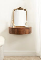 Curved floating wood side table with a decorative wooden-framed mirror above, styled with perfume bottles and a phone on top, against a white wall and curtain.