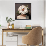Framed canvas portrait of a woman with a large white flower obscuring her face, set against a dark background, hanging above a wooden desk with beige chair.