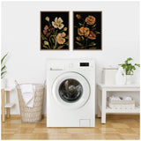 Two framed floral art prints with muted orange and cream flowers on black backgrounds, hanging above a white front-load washer in a laundry room.