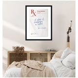 Framed print of a prescription note featuring script "A glass of champagne as needed" on a beige wall above a wooden cabinet with dried plants and a cozy bed with white and beige linens.